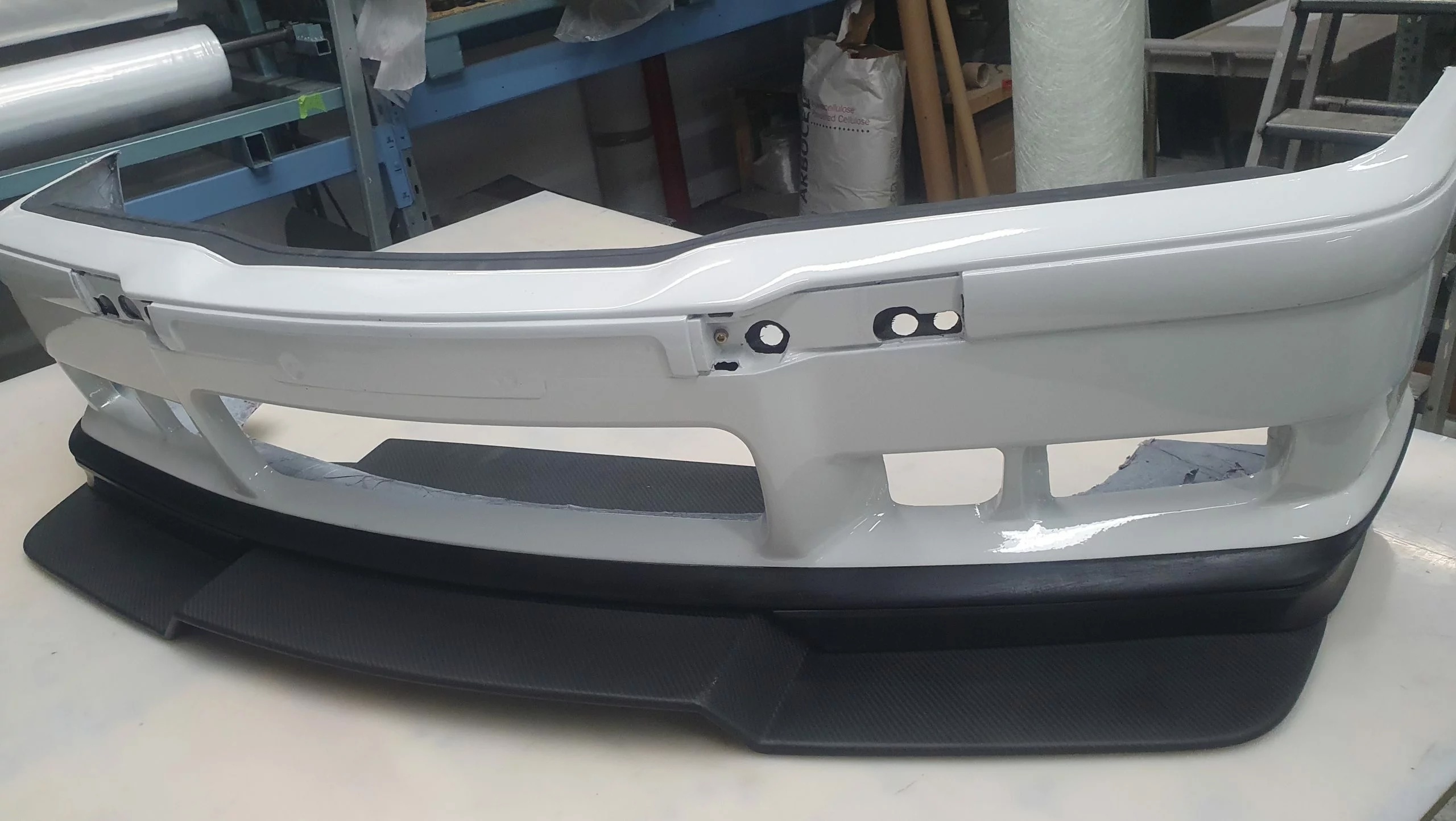 BMW E36 Frontstoßstange mit Carbon-Frontsplitter montiert, Rennfahrzeug im Werkstattumfeld