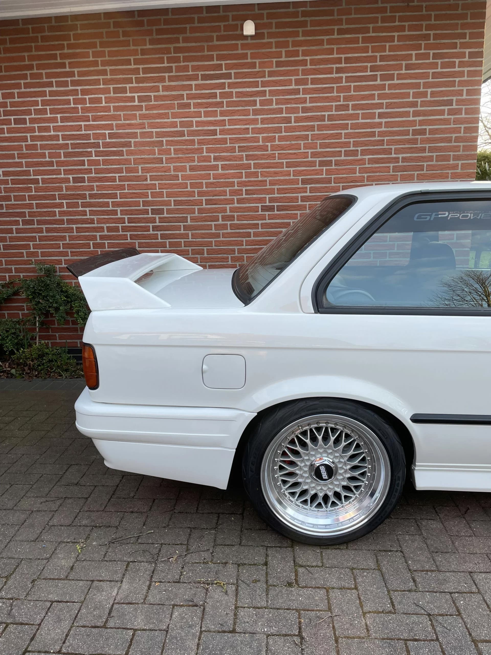 Seitenansicht eines weißen BMW E30 mit montiertem Heckspoiler am Kofferraum.