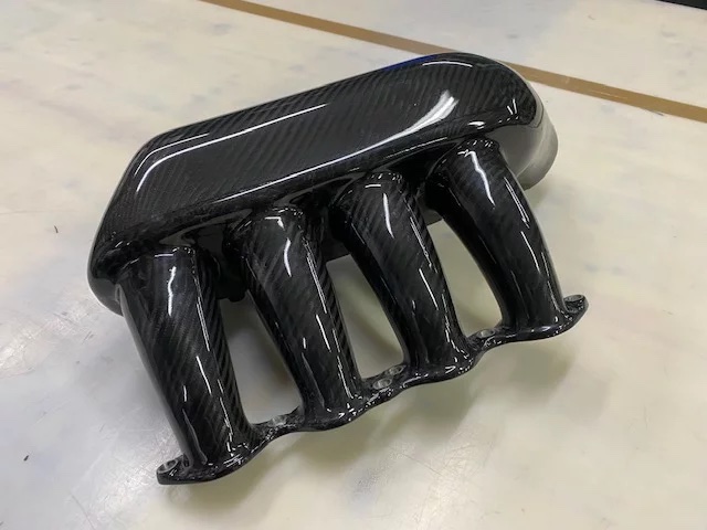 Carbon-Ansaugplenum (Airbox) in Hochglanz-Carbonoptik mit vier Ansaugrohren/Runnern und Befestigungsflansch, Detailansicht schräg von vorn