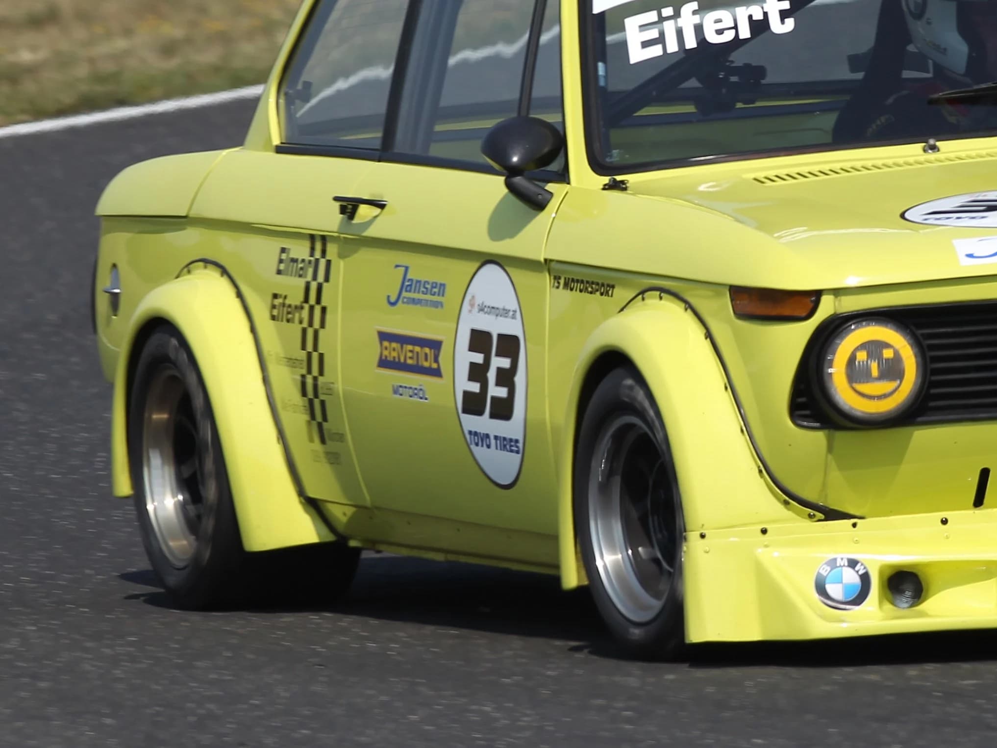 Gelber BMW E10 auf der Rennstrecke mit Detailaufnahme vom Carbon Verbreiterungssatz an der Beifahrerseite