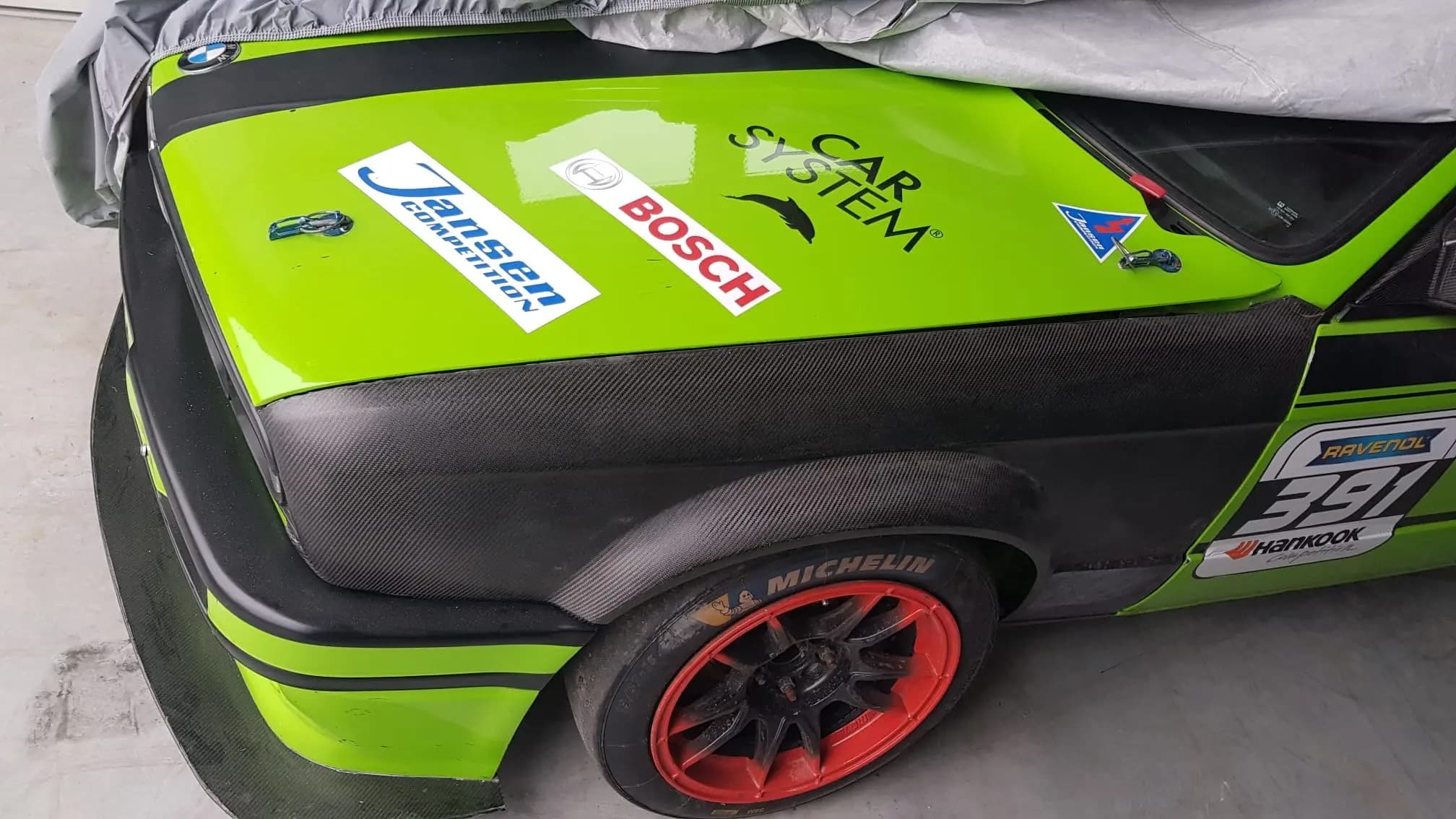 Breiter Carbon-Kotflügel für BMW E30, montiert an Rennfahrzeug mit verbreitertem Radlauf und Slickbereifung
