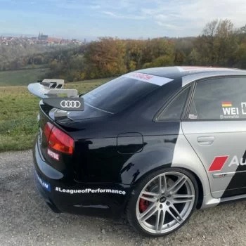 Audi RS4 Rennfahrzeug schräg hinten – Schwarzer Audi RS4 mit Carbon-Heckflügel und Rennbeklebung im Außenbereich