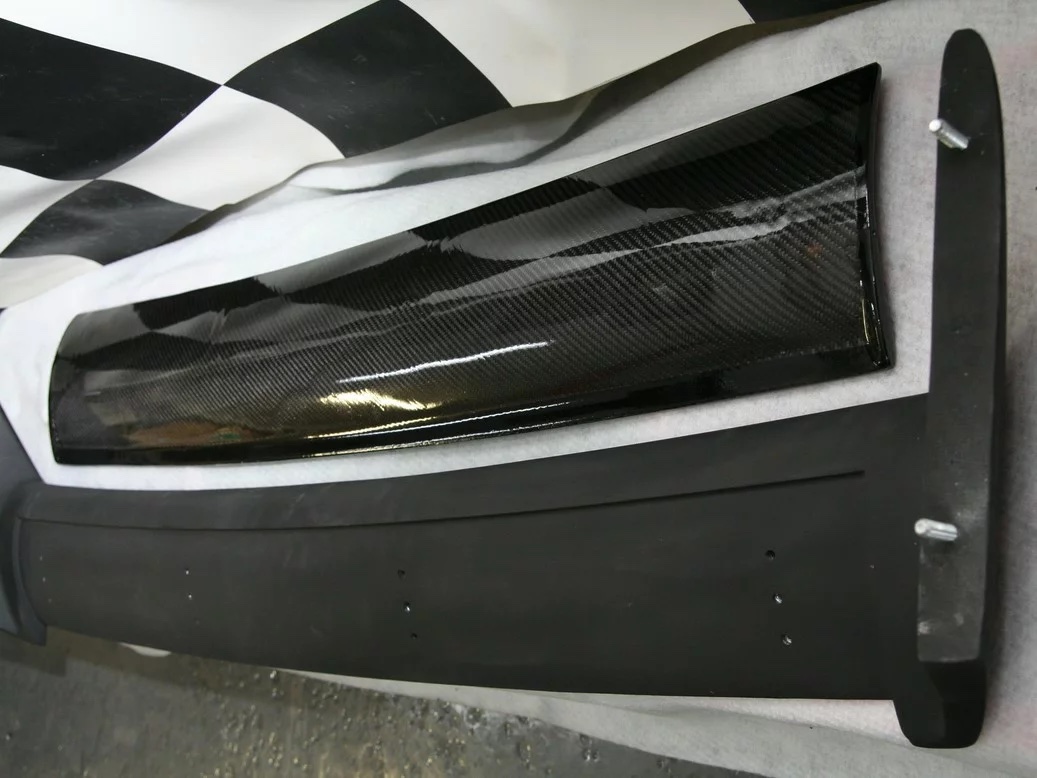 BMW E30 M3 Heckspoiler-Set: matte Spoilerbasis mit glänzendem Sichtcarbon-Element, Detailansicht der Seitenfläche.