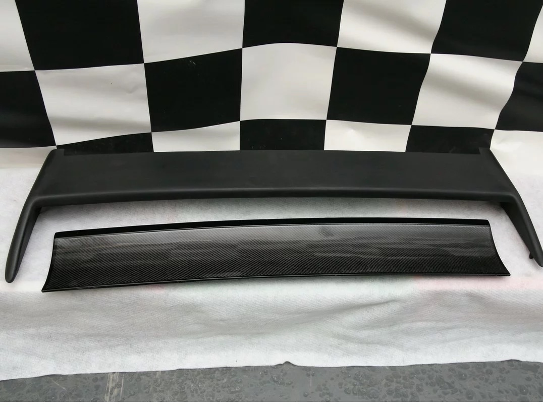 BMW E30 M3 Heckspoiler in zwei Teilen – matte Spoilerbasis und Sichtcarbon-Blende – frontale Ansicht auf weißer Unterlage.
