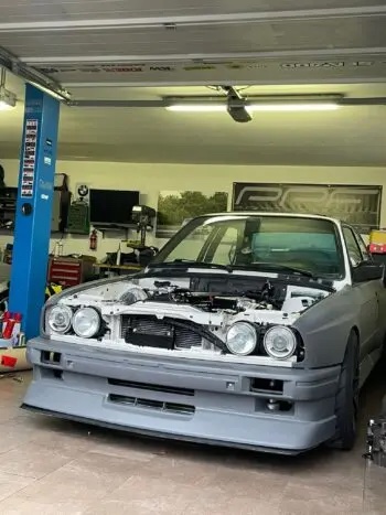 BMW E30 ohne Motorhaube in der Werkstatt von vorne mit Blick auf den Frontspoiler Cecetto von rechts