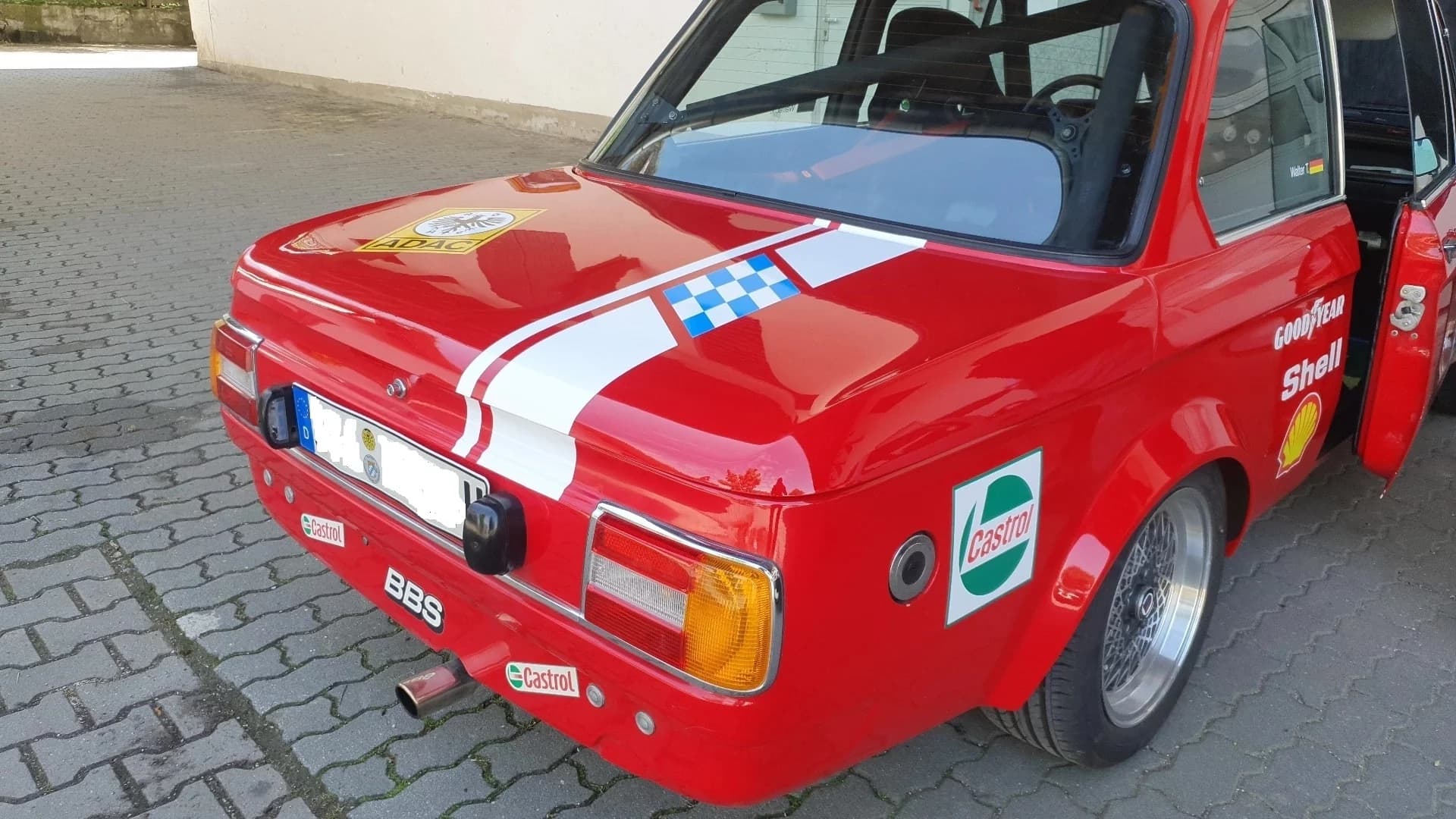 Roter BMW E10 1502-2002 Alpina steht auf einem Hof mit der Nahaufnahme auf den geschlossenen Kofferraumdeckel