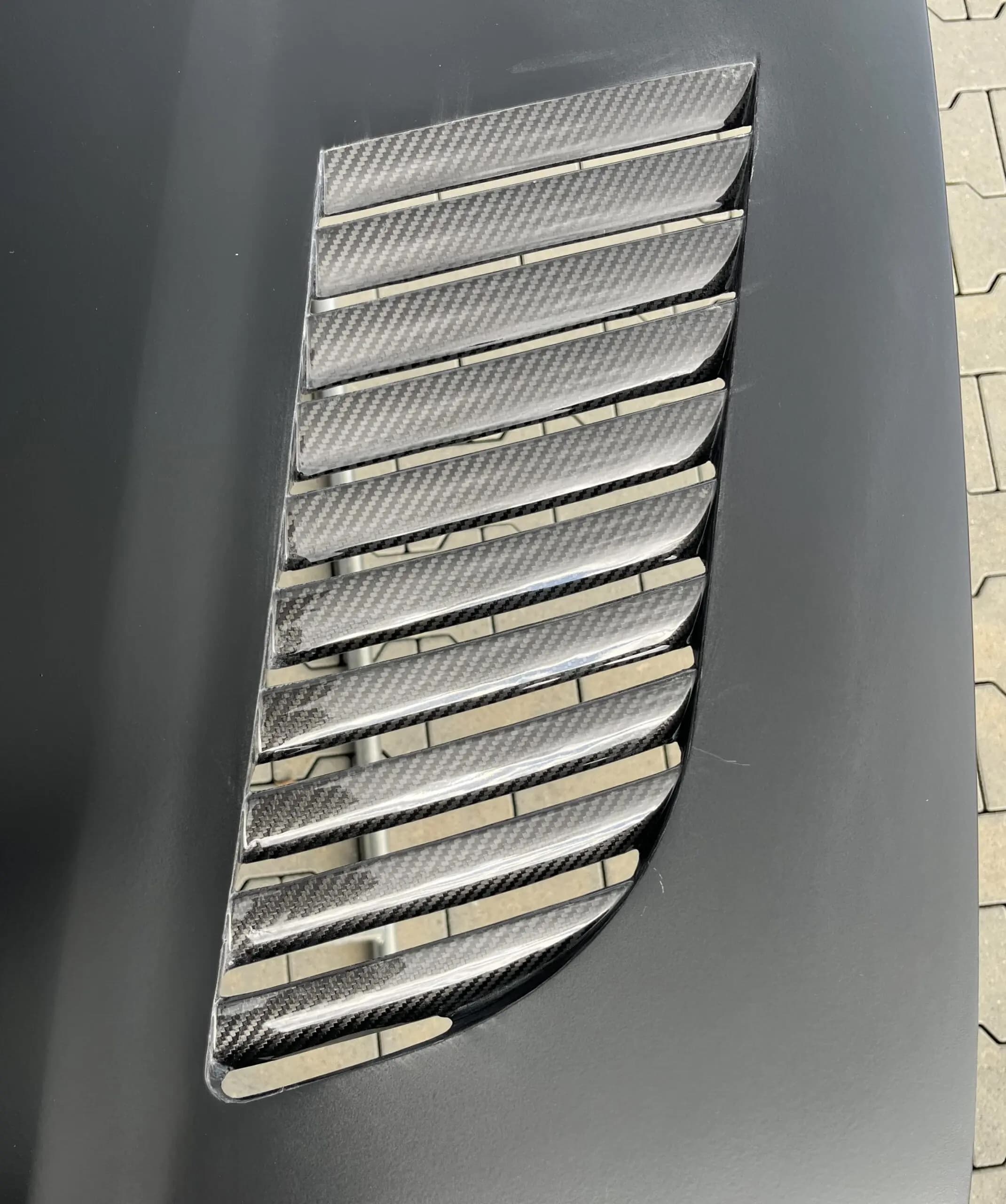 Carbon-Luftauslass mit schrägen Lamellen in schwarzer Motorhaube