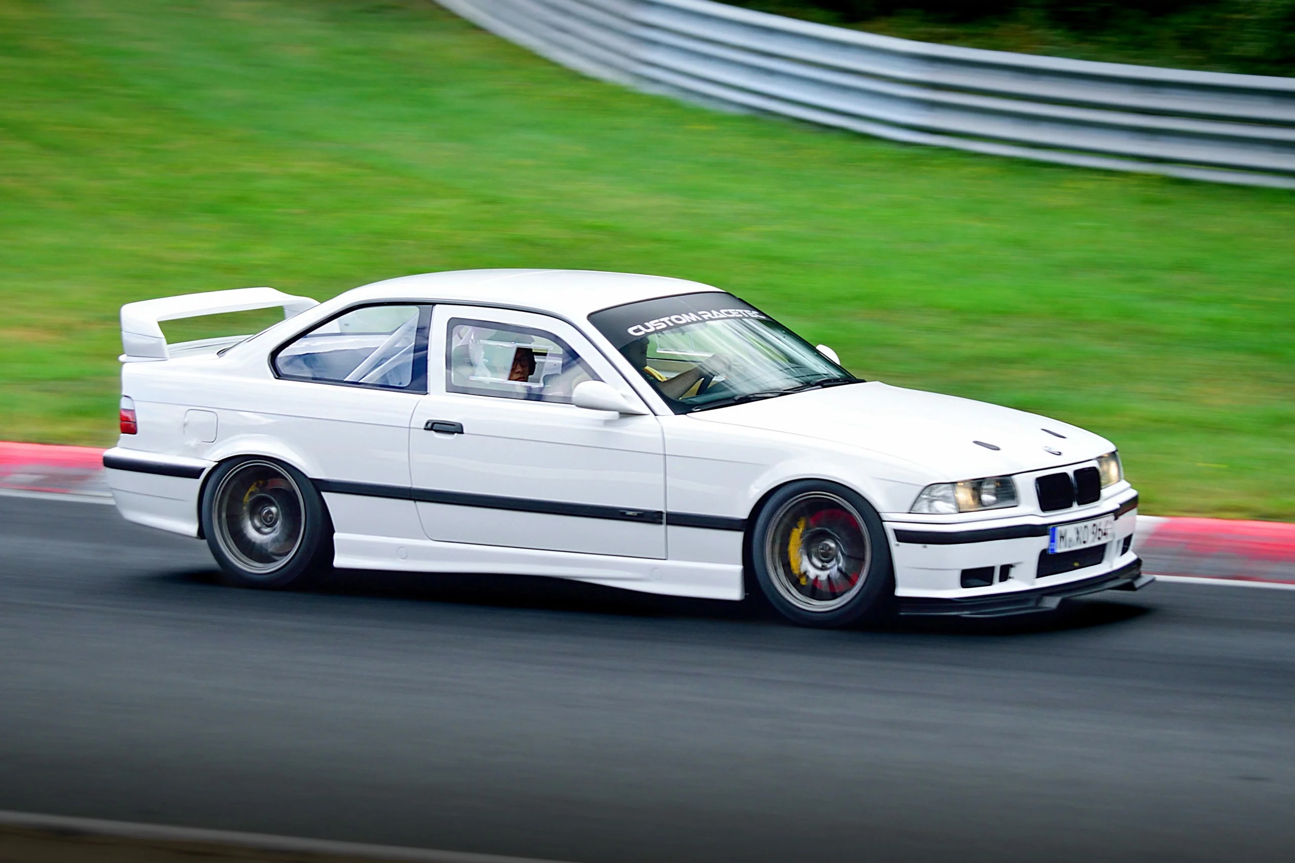 BMW E36 Coupe Seitenansicht auf der Rennstrecke, tiefergelegt mit Überrollkäfig und Heckspoiler