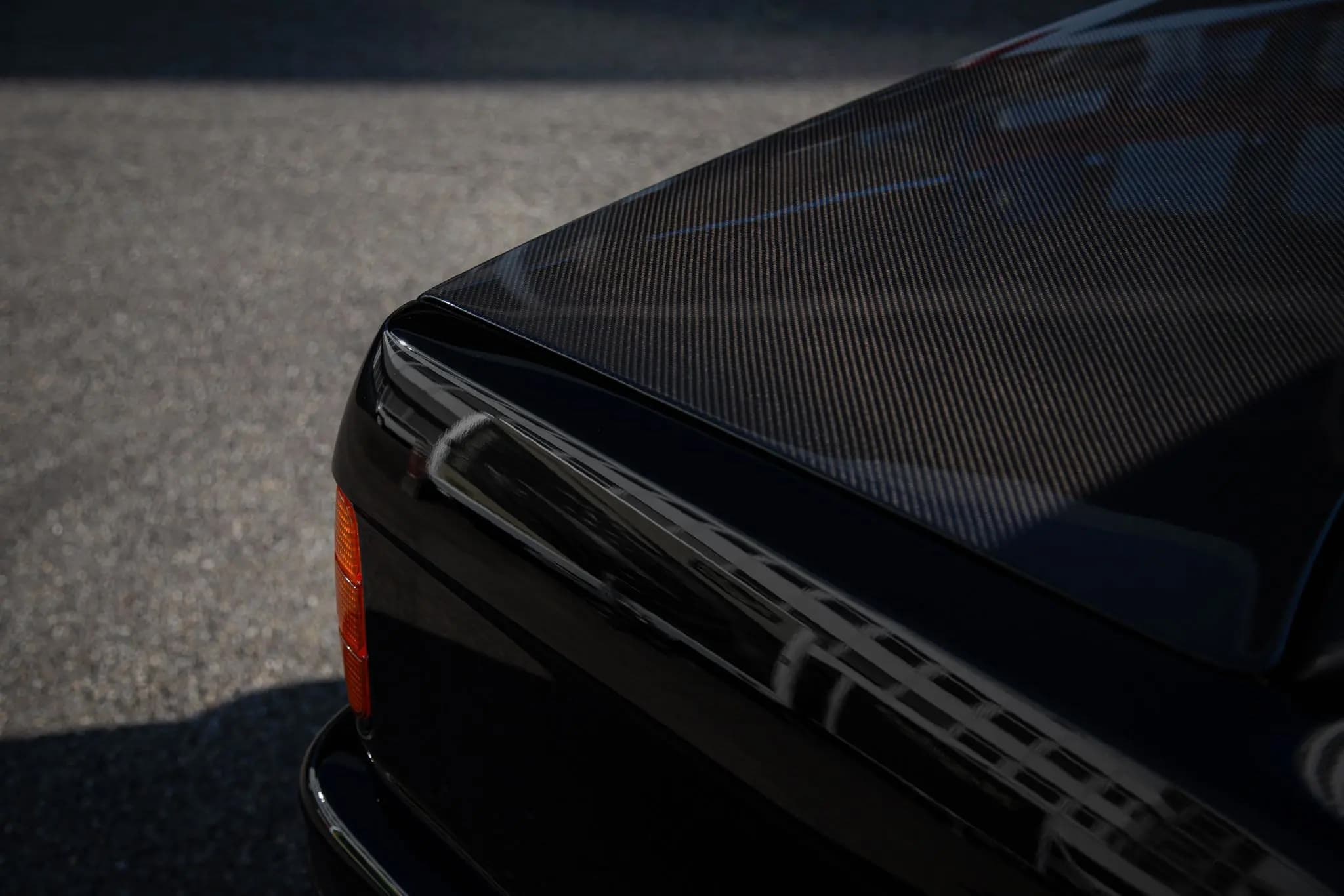 Detailaufnahme der Ecke eines Sichtcarbon-Kofferraumdeckels am BMW E30 mit glänzender Oberfläche und Carbongewebe.