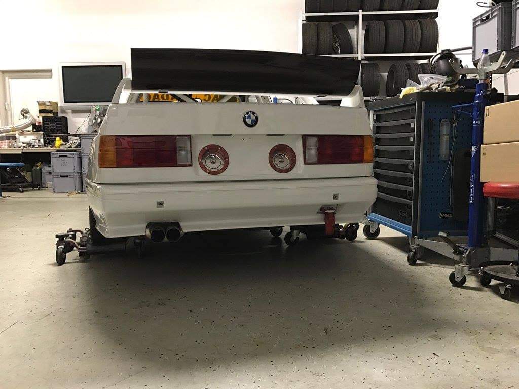 Gerade Heckansicht in der Werkstatt: BMW E30 mit großem Heckflügel auf dem Kofferraumdeckel.
