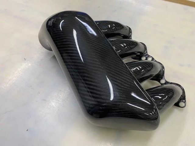 Hochglanz Carbon-Airbox/Ansaugplenum von oben, mit vier Ansaugkanälen (Runnern) und sichtbaren Montage-/Flanschbohrungen, Motorsport-Komponente