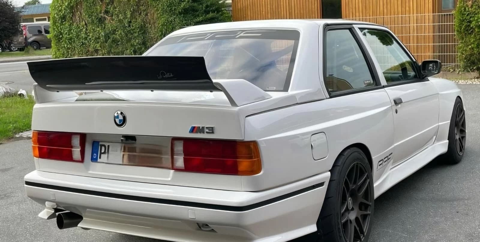 Hintere Dreiviertelansicht eines weißen BMW E30 mit montiertem Heckspoiler und breiter Flügelkante.
