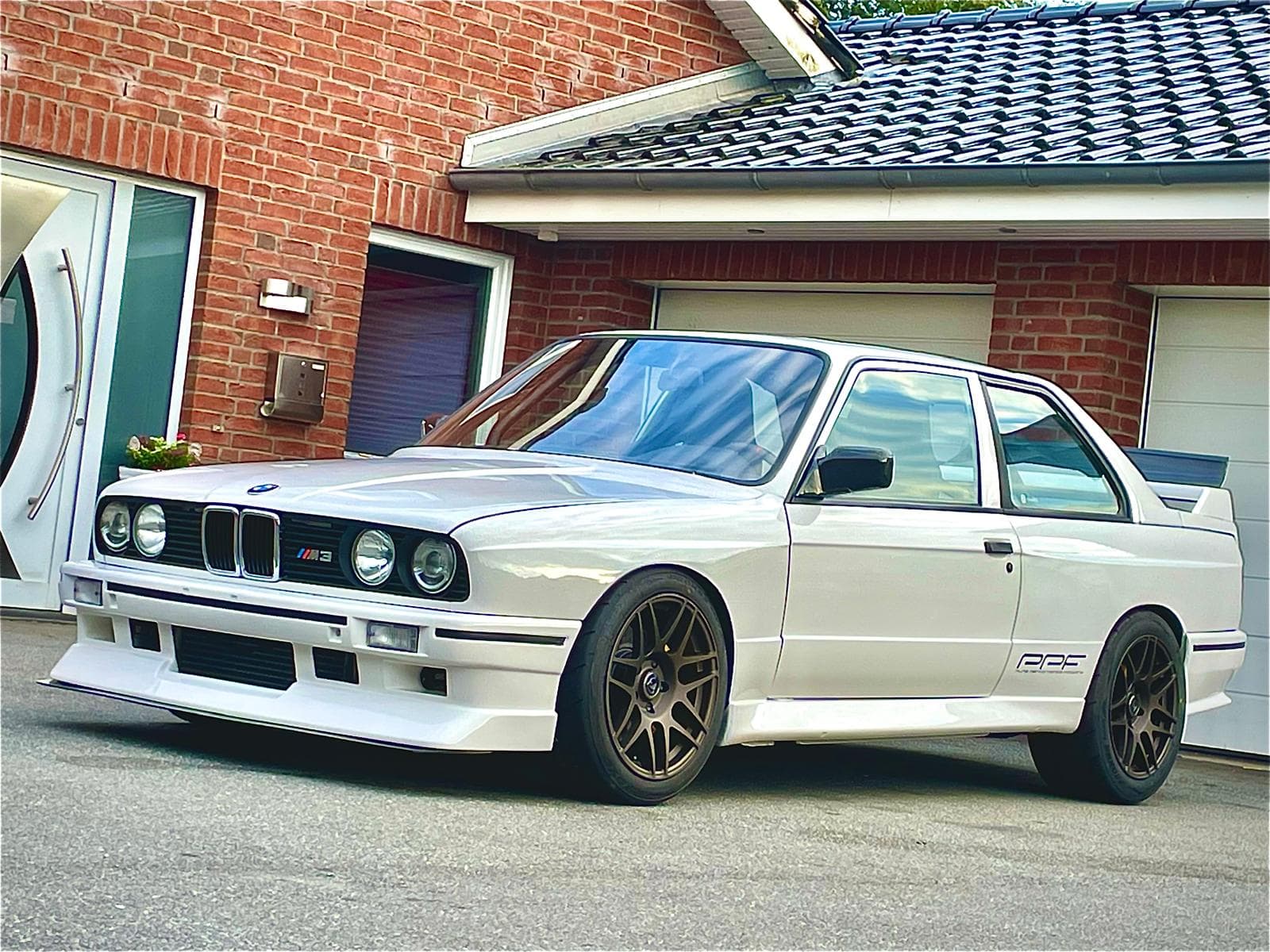 BMW E30 M3 mit montierten Carbon-Kotflügeln – schräge Seitenansicht vor Garage